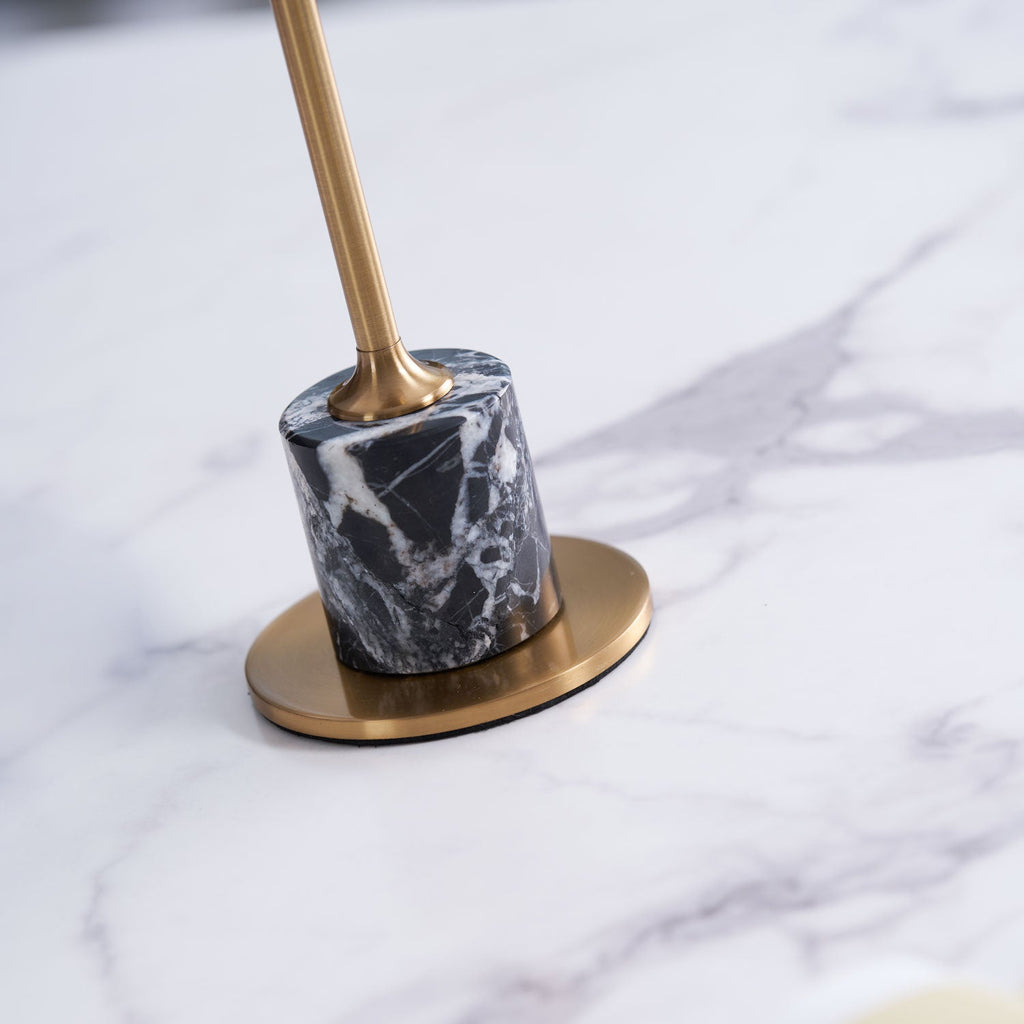 Macro close-up of the marble base and brass foot plate on a Clérachic table lamp, its stem blurred out of focus above.