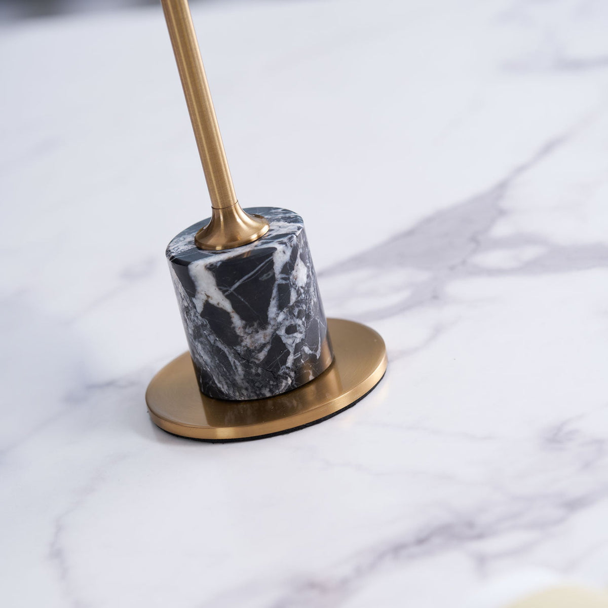 Macro close-up of the marble base and brass foot plate on a Clérachic table lamp, its stem blurred out of focus above.