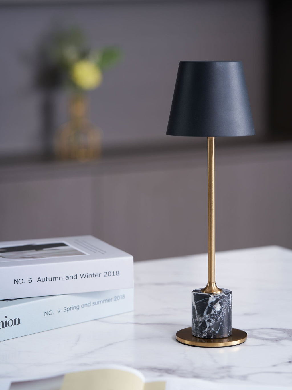 The same Clérachic marble-tabletop scene from a wider crop, the lamp glowing beside stacked magazines and an open book.