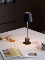A Clérachic marble table lamp lights a marble tabletop with an open magazine and dried branch, warm light across the scene.