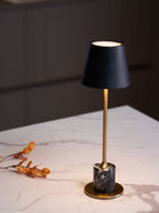 A Clérachic marble table lamp glows on a marble counter in a dark kitchen setting, a dried orange branch resting beside its base.
