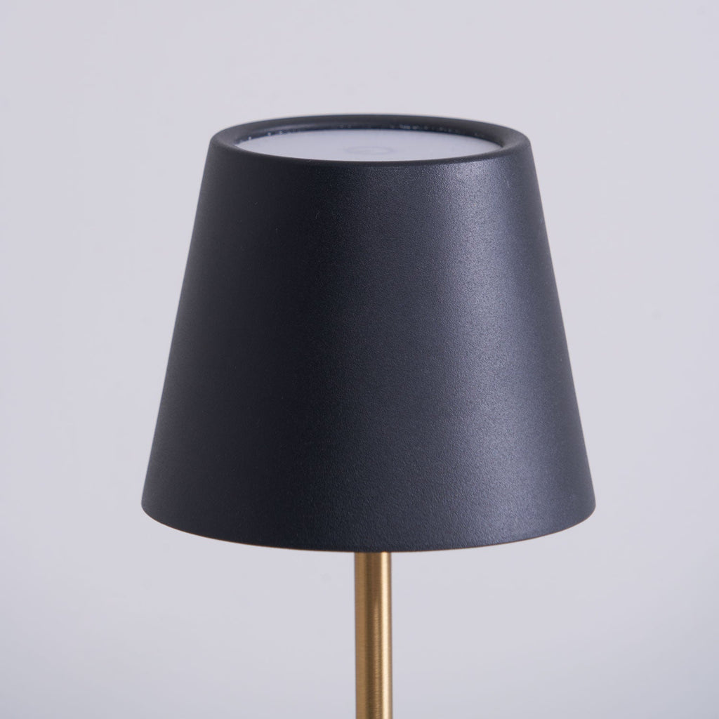 Close-up of the black conical shade on a Clérachic marble table lamp, its open top rim and brass rod visible against grey.
