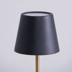 Close-up of the black conical shade on a Clérachic marble table lamp, its open top rim and brass rod visible against grey.