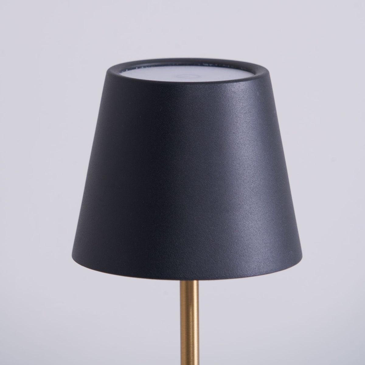 Close-up of the black conical shade on a Clérachic marble table lamp, its open top rim and brass rod visible against grey.