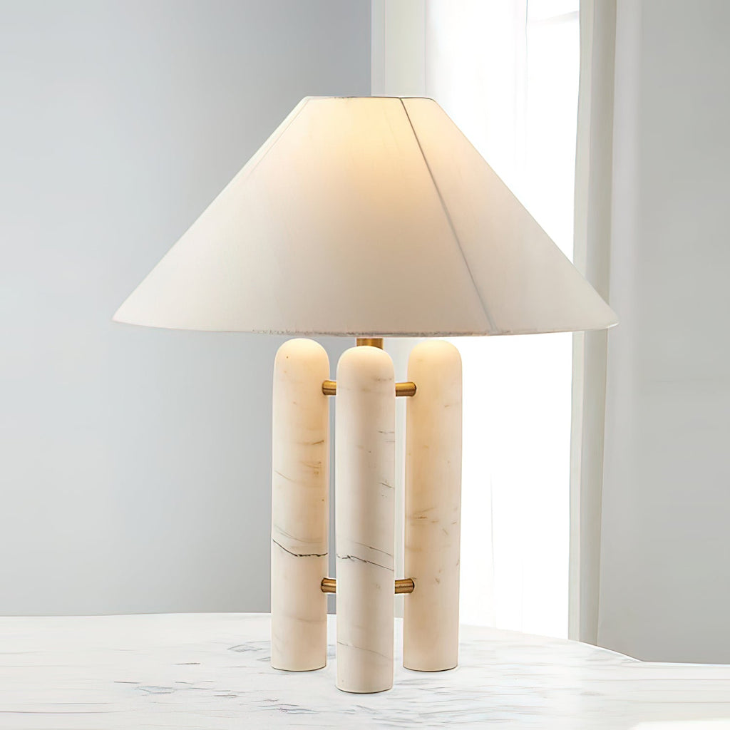 Marble-column table lamp by Clérachic lit on a white marble table, soft daylight filtering through a sheer curtain.