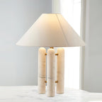 Marble-column table lamp by Clérachic lit on a white marble table, soft daylight filtering through a sheer curtain.