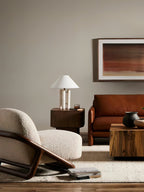 Clérachic table lamp glowing on a distant side table in a full living-room view with a rust leather chair.