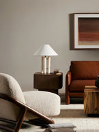 Clérachic table lamp on a dark wood side table in a living room, a cream bouclé armchair and rust sofa nearby.