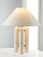 Clérachic table lamp glowing warmly on the marble table, its wide shade half-lit against the curtained window.