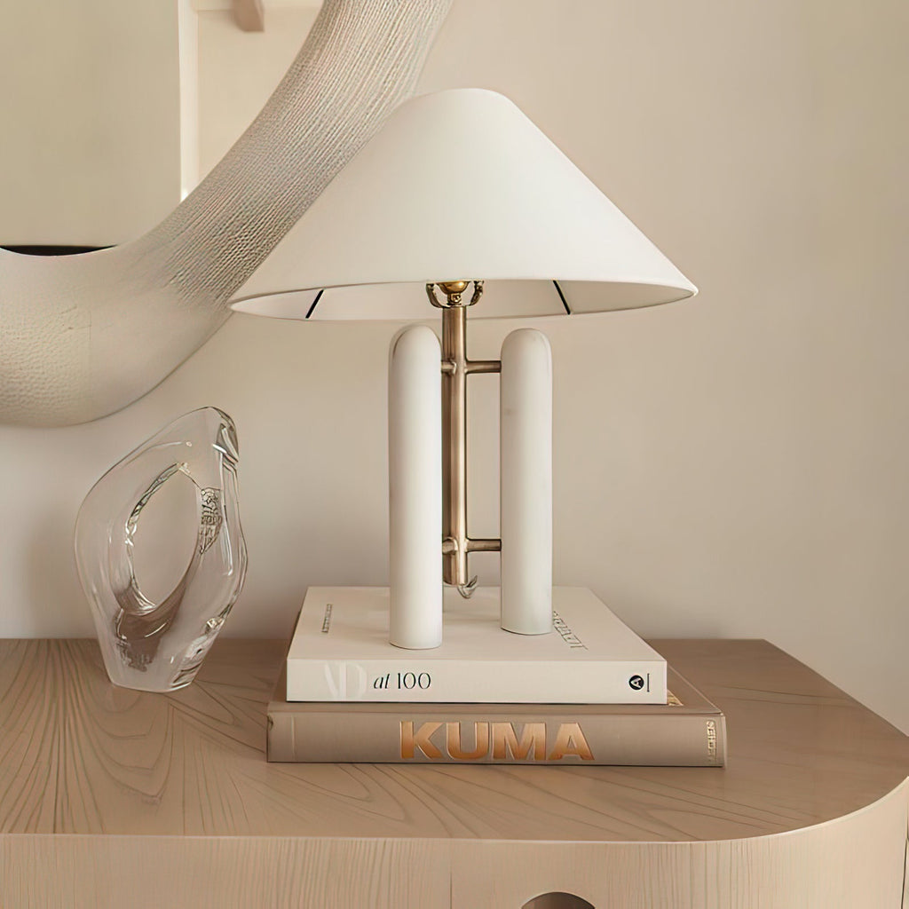 Clérachic table lamp on a stack of books beside a clear glass vase on a light wood nightstand.