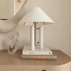 Clérachic table lamp on a stack of books beside a clear glass vase on a light wood nightstand.