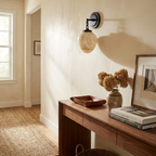 In a hallway, this Clérachic wall sconce in black finish hangs above a walnut console table with dried flowers.