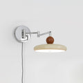 Round disc wall lamp glowing warmly beside a bed