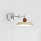 Round disc wall lamp glowing warmly beside a bed