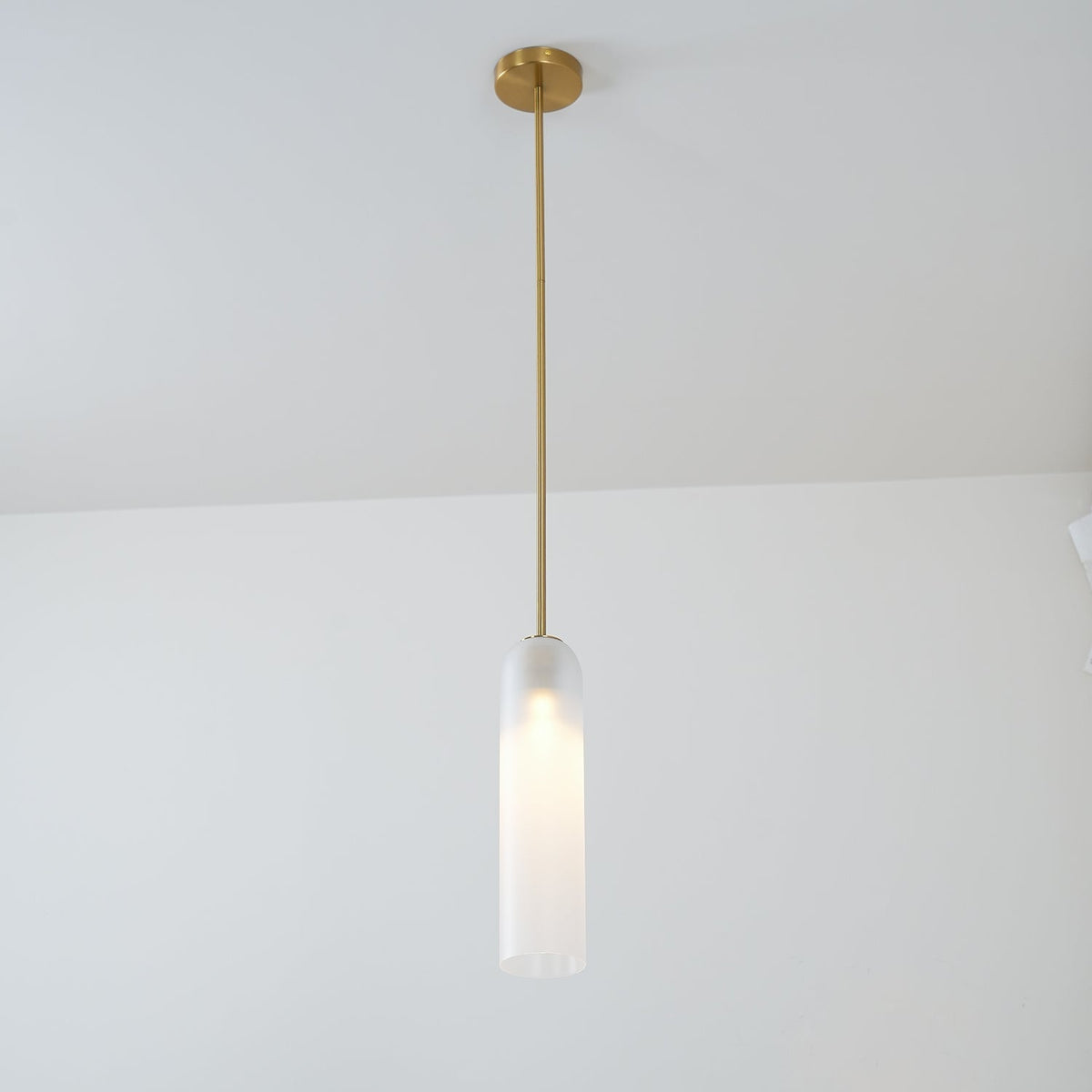 A single pendant of this Clérachic light in white glass hangs from a gold rod in a plain room corner.