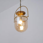 Amber glass cup pendant light with gold frame on a plain background