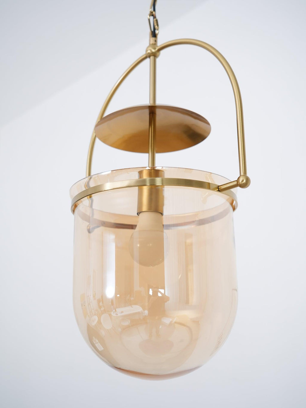 Amber glass cup pendant light with gold frame viewed at an angle