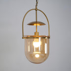 Amber glass cup pendant light with gold frame hanging over a table