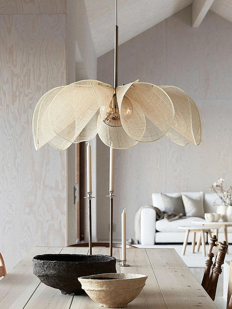 In a room with a vaulted, wood-plank ceiling, this Clérachic pendant's beige fiber petals hang above a wood table set with dark ceramic bowls.