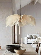In a room with a vaulted, wood-plank ceiling, this Clérachic pendant's beige fiber petals hang above a wood table set with dark ceramic bowls.