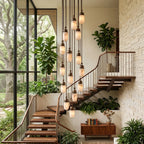 Alongside a wood staircase and potted greenery, this Clérachic pendant's capsules cascade down the stairwell in a tall run.