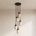 Staggered at different lengths, this Clérachic pendant's alabaster capsules glow warm against a plain wall backdrop.