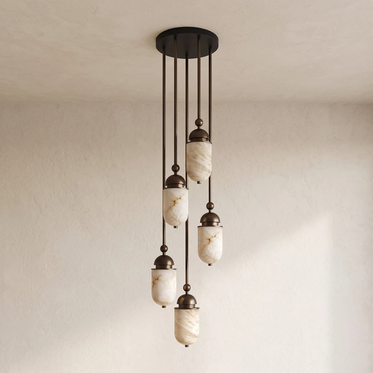 Staggered at different lengths, this Clérachic pendant's alabaster capsules glow warm against a plain wall backdrop.