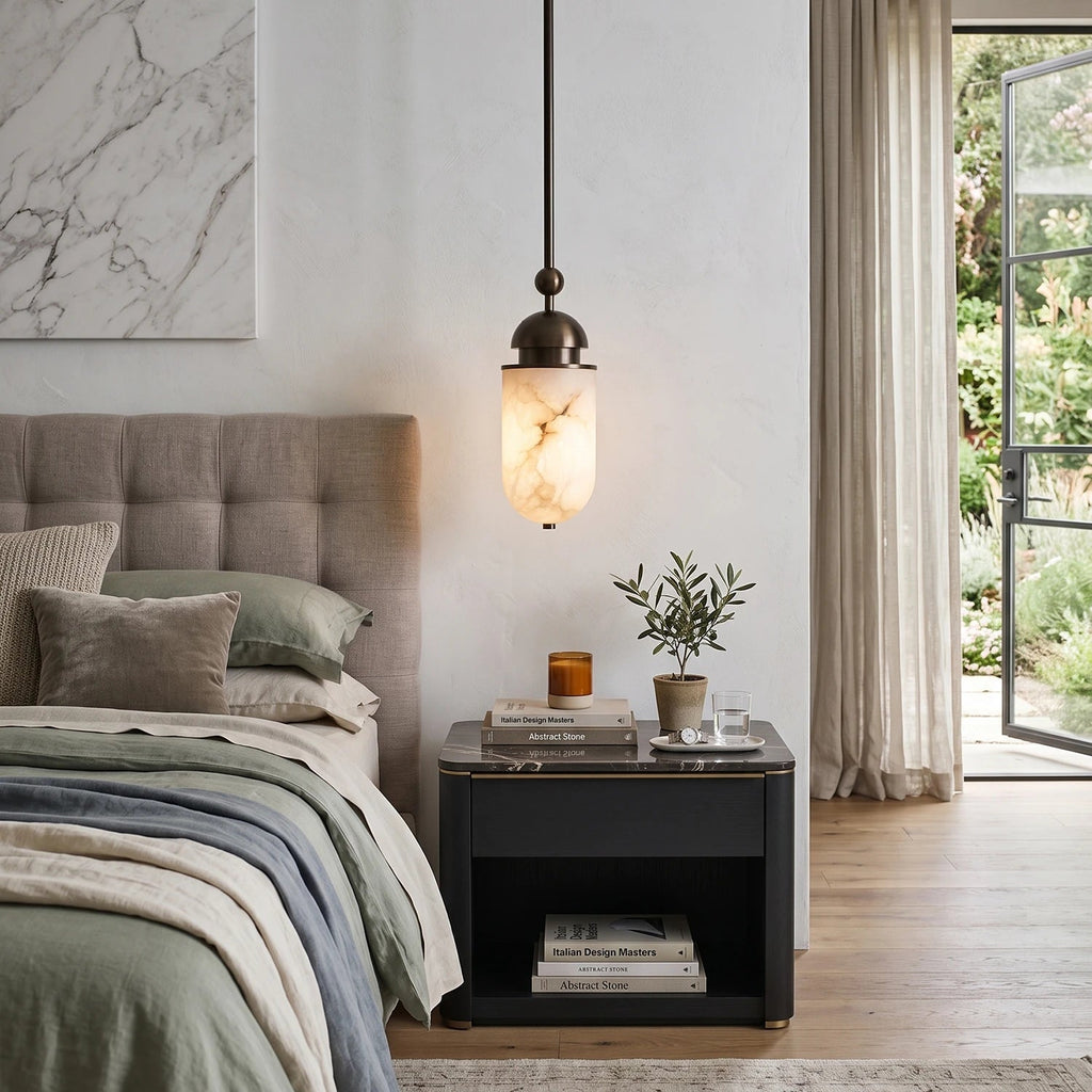 A single alabaster capsule from this Clérachic pendant glows warm beside a bed with a tufted headboard and nightstand.