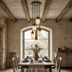 Beneath a wood-beamed vault and arched window, this Clérachic pendant's alabaster capsules glow over a set dining table.