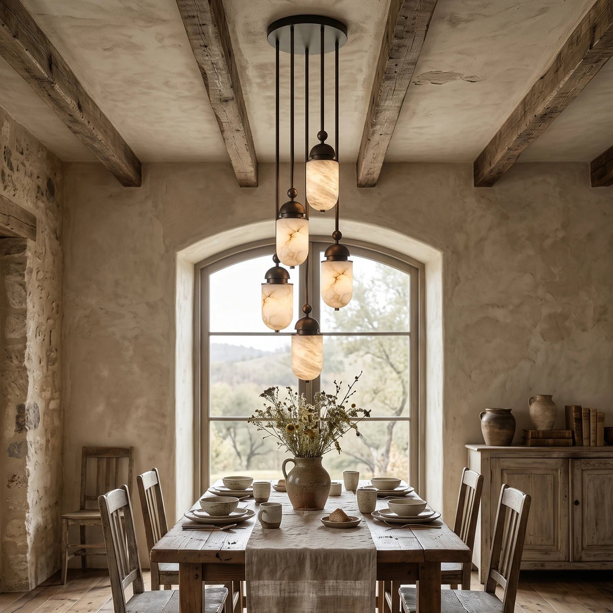 Beneath a wood-beamed vault and arched window, this Clérachic pendant's alabaster capsules glow over a set dining table.