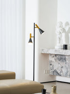 Black and brass Clérachic floor lamp positioned by a marble fireplace mantel with a small statue ornament nearby.