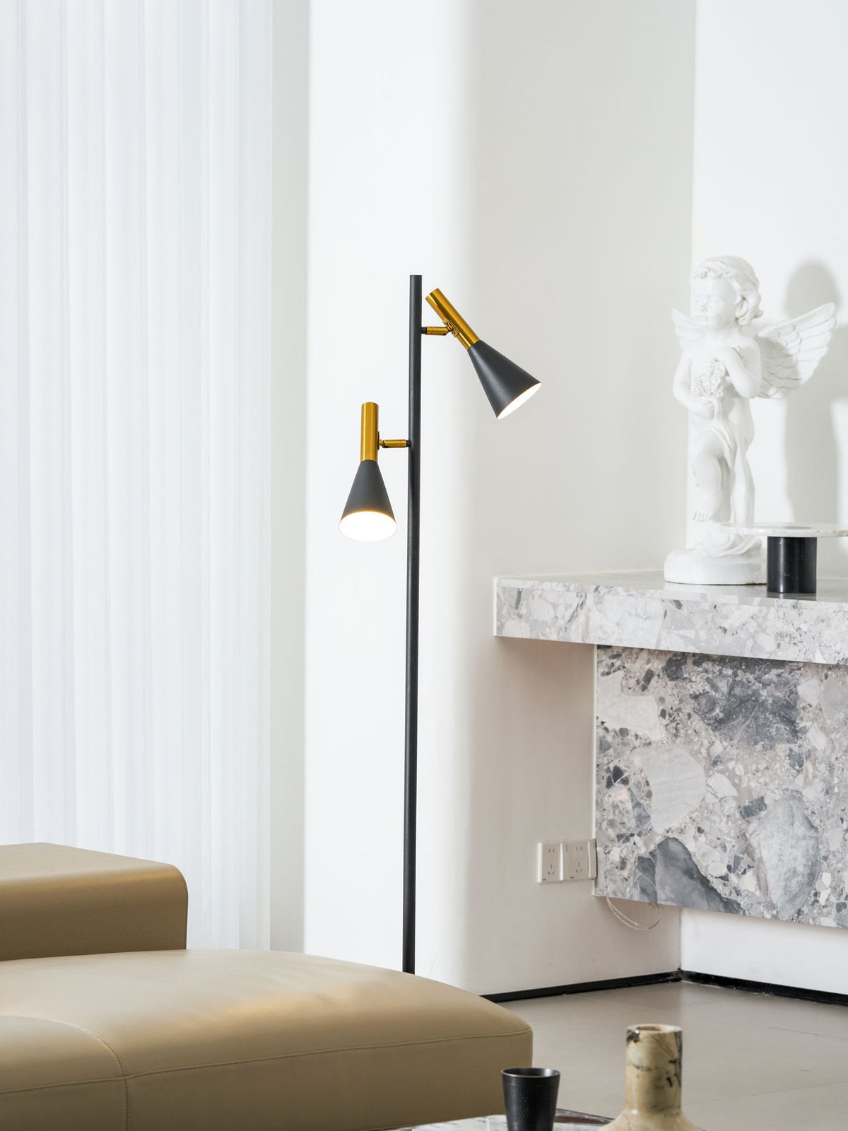 Black and brass Clérachic floor lamp positioned by a marble fireplace mantel with a small statue ornament nearby.