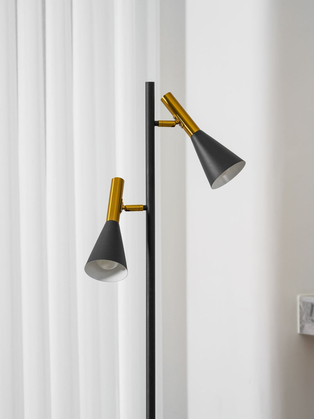 Cropped close view of the two shade heads on a black Clérachic floor lamp beside a curtained window and marble wall.
