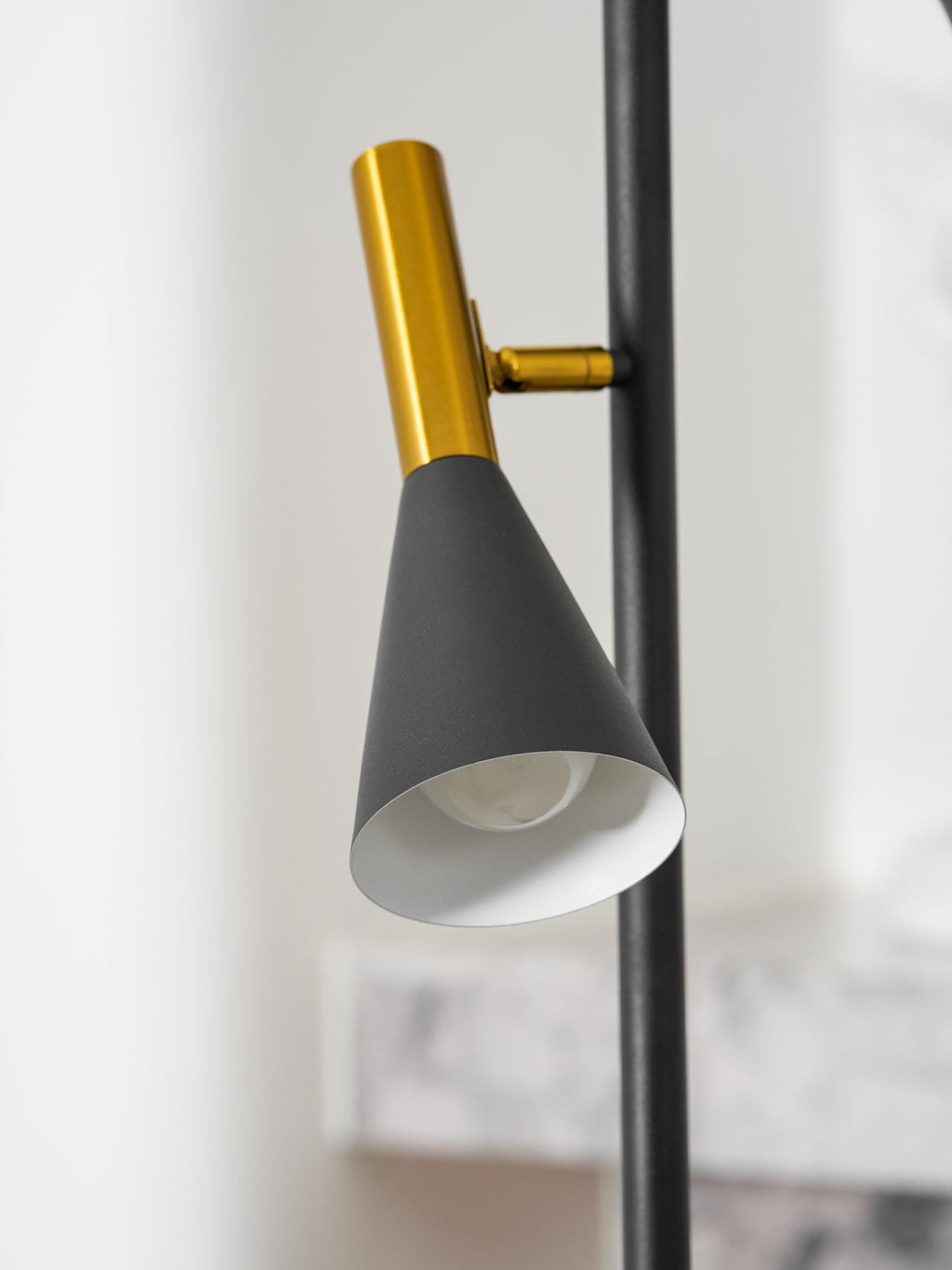 Extreme close-up of one brass neck and cone shade on a Clérachic floor lamp, the white interior of the shade visible.