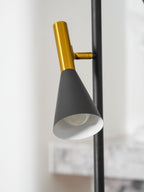 Extreme close-up of one brass neck and cone shade on a Clérachic floor lamp, the white interior of the shade visible.
