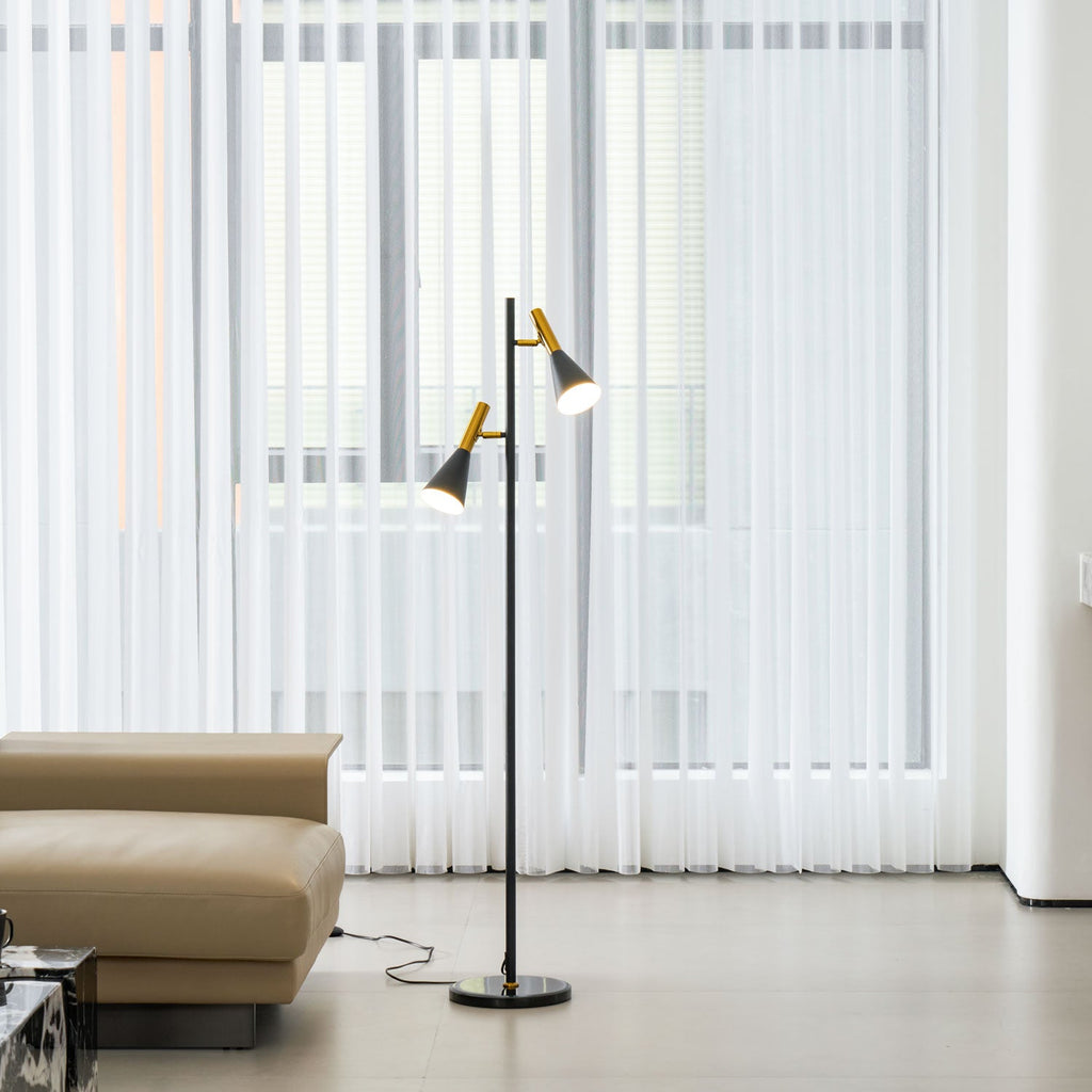 Sheer curtains fill the window beside a beige leather chaise and a black and brass Clérachic floor lamp close by.