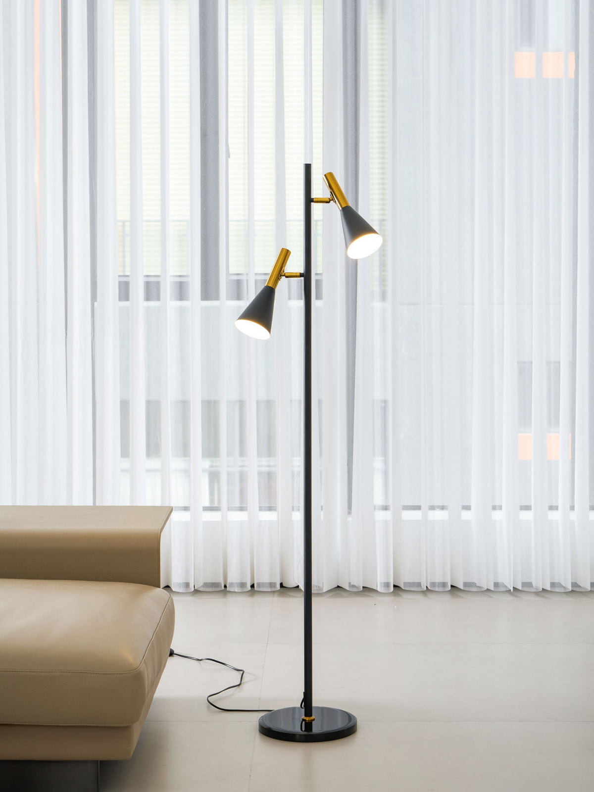 A building outline shows through sheer curtains, seen further back in the room with a black and brass Clérachic floor lamp.