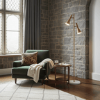 Brass Clérachic floor lamp against a grey stone wall, beside a green velvet armchair with a folded throw.