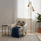 Brass Clérachic floor lamp on a marble base beside a cream armchair holding a navy throw, with a potted plant near.