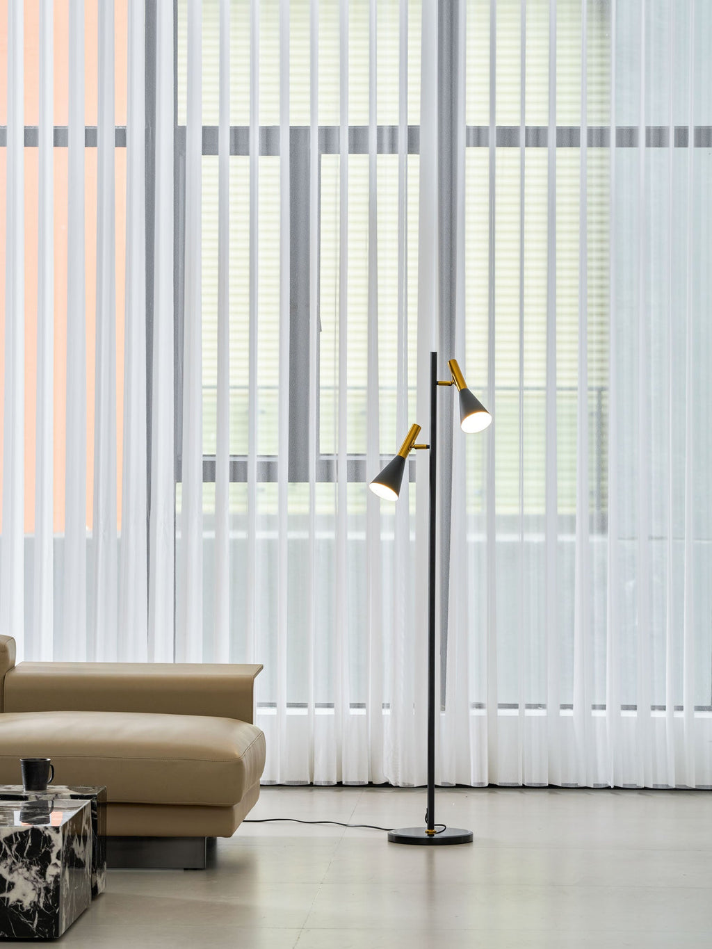 Black Clérachic floor lamp standing near sheer curtains and a beige ottoman, a dark marble side table cropped in frame.