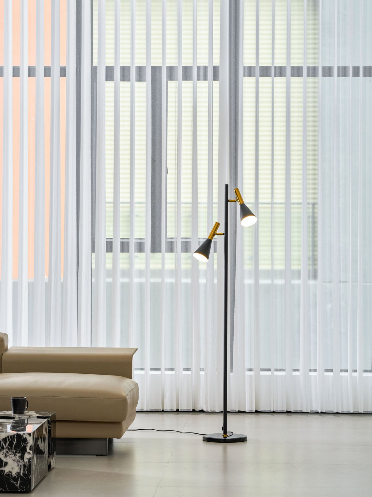 Black Clérachic floor lamp standing near sheer curtains and a beige ottoman, a dark marble side table cropped in frame.