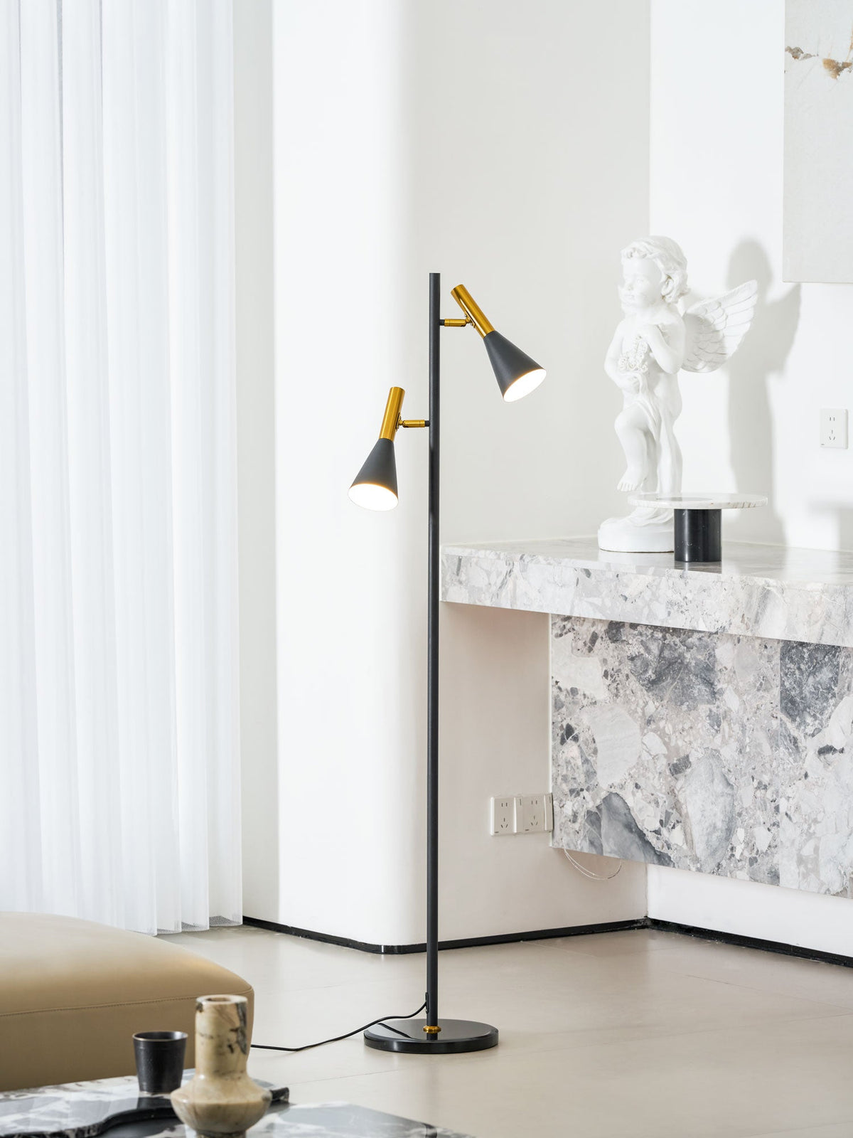 A small statue tops a marble console table beside a black and brass Clérachic floor lamp, a sheer curtain behind.