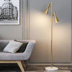 Brass-finish Clérachic two-head floor lamp beside a grey sofa, its angled shades lit warm under a framed street print.