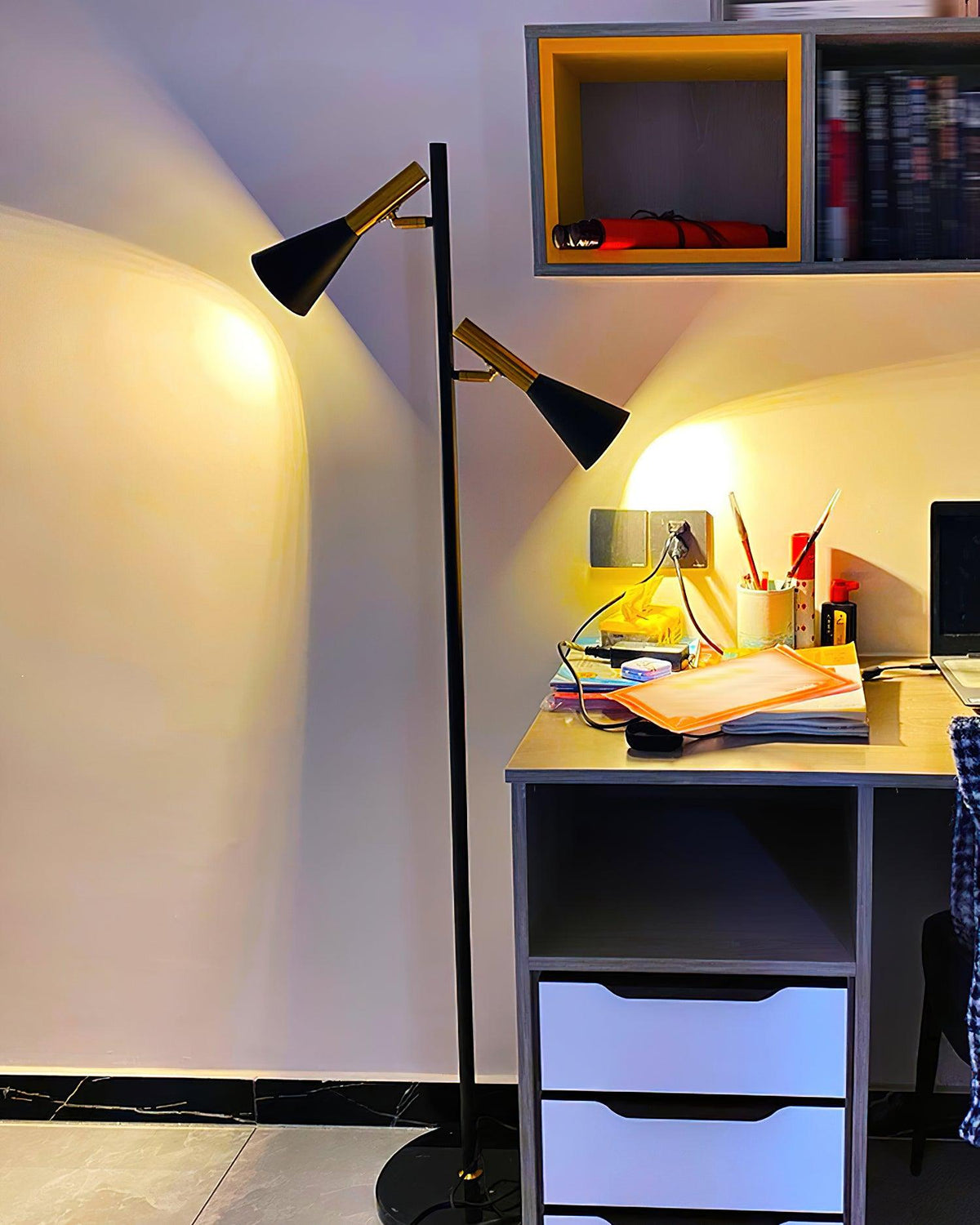 A home-office desk with open shelving cubbies sits beside a black and brass Clérachic floor lamp glowing warm.