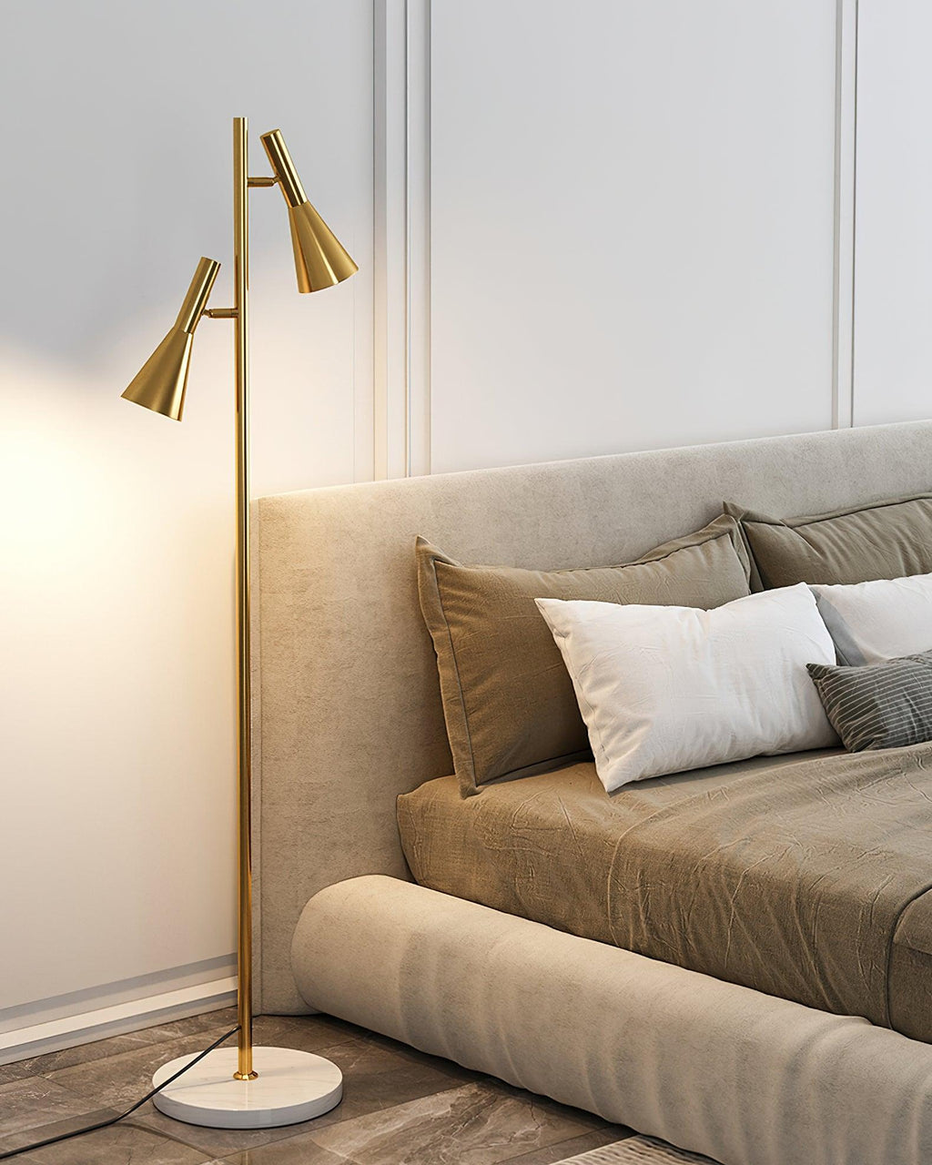 A beige upholstered bed with white pillows sits beside a brass Clérachic floor lamp glowing warm on its marble base.
