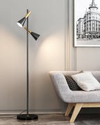 A framed black-and-white print hangs behind a beige tufted sofa lit warm by a black and brass Clérachic floor lamp.