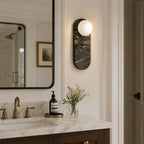A single black marble Clérachic sconce lights the wall beside a black-framed mirror in a light wood vanity setting.