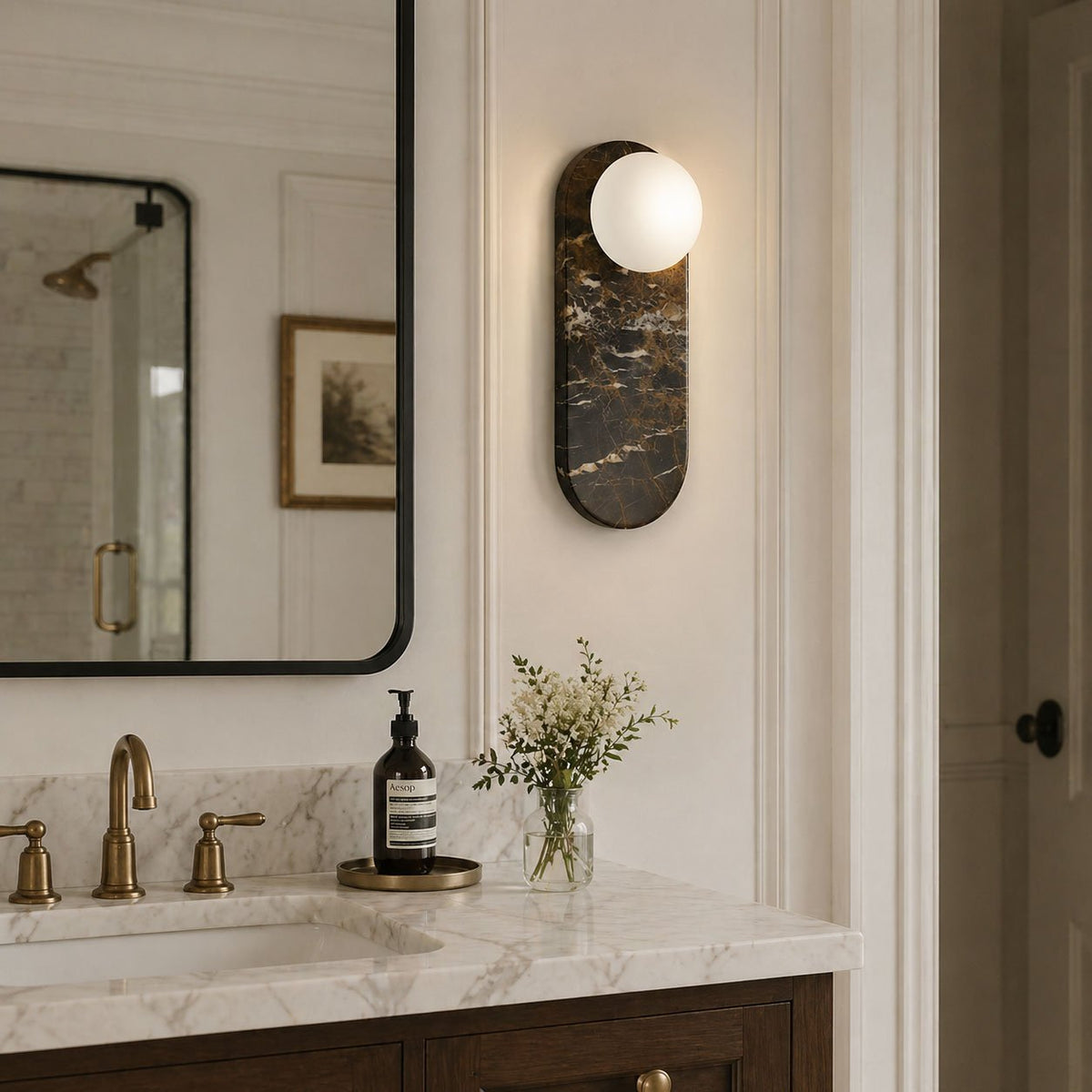 A single black marble Clérachic sconce lights the wall beside a black-framed mirror in a light wood vanity setting.