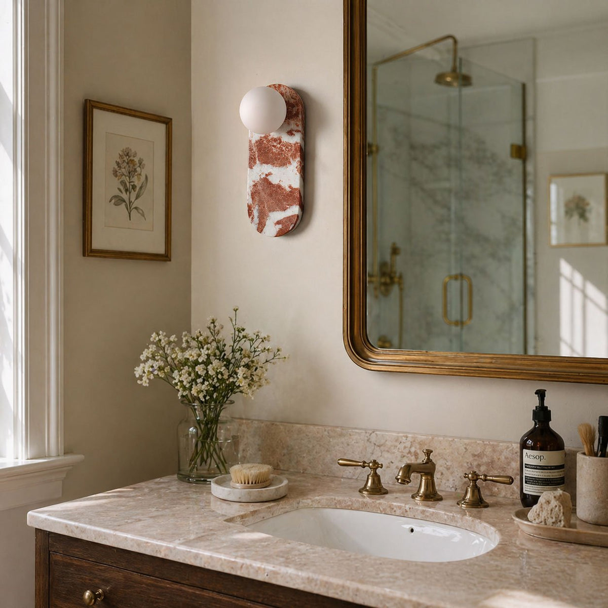 The red-veined Clérachic sconce glows beside a gilt-framed mirror, with a glass shower and dried flowers nearby.