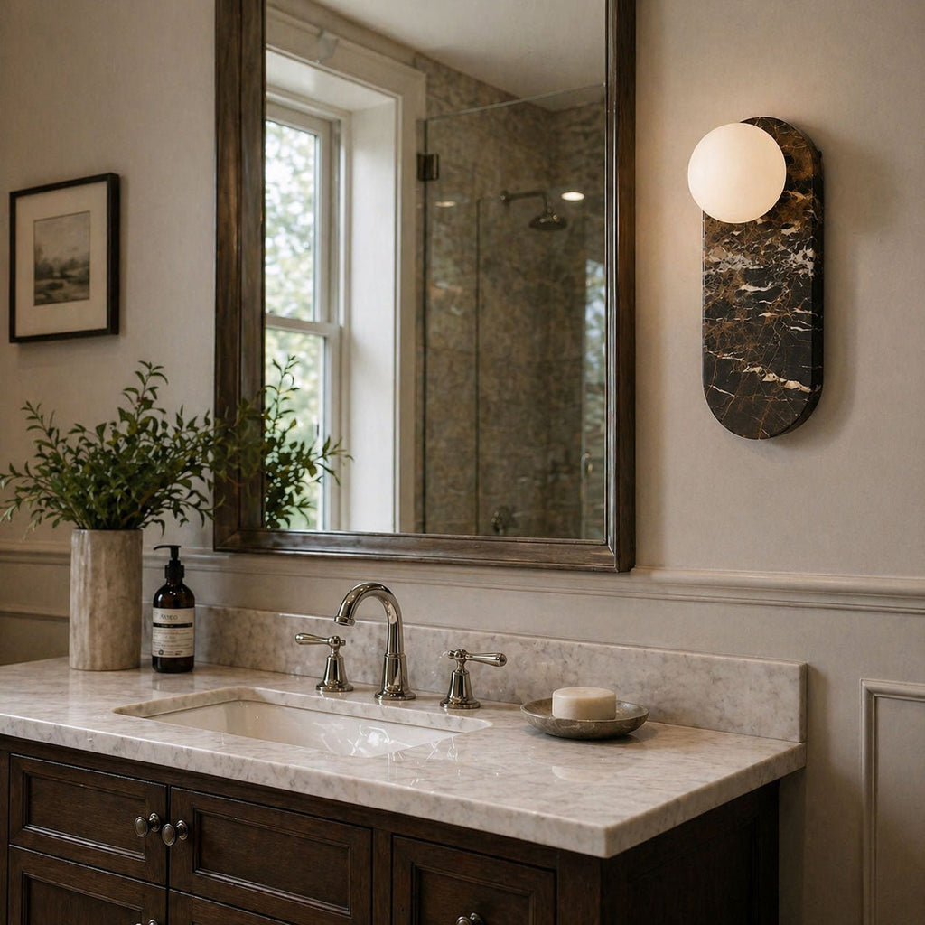 Beside a window, the dark marble Clérachic sconce lights a vanity with a potted plant and a glass shower stall.
